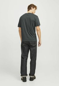 Tumši pelēks īsām piedurknēm T-krekls, kokvilnas maisījums, apaļa kakla izgriezums. Apvienots ar tumšas džinsu biksēm, kurām ir dzeltena šuvuma un izlocīti šorti. Melna apavošana.