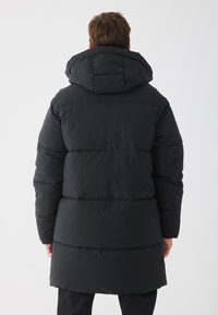 Sort pufferjakke med hætte, udstyret med en quiltet design og synlige vandrette syninger. Fremstillet af blødt, isoleret materiale.