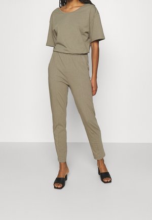 Completo in due pezzi khaki composto da una maglietta larga con scollatura ampia e pantaloni slim-fit con vita elasticizzata, abbinato a scarpe nere senza lacci.