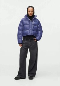 Casaco puff vermelho curto com um acabamento brilhante, fecho com zíper e capuz, combinado com jeans pretos de perna larga e botas pretas robustas.