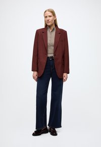 Blazer oversize couleur bordeaux, top beige ajusté, jean à jambes larges bleu foncé, et mocassins marron. Le blazer présente un col cranté et une poche poitrine unique.
