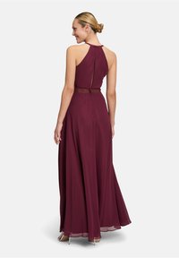 Robe de soirée bordeaux avec un col halter, une jupe fluide et une taille texturée. Dotée d'une ouverture discrète au dos.