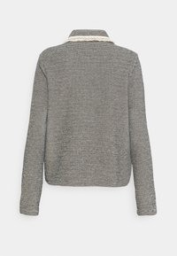 Chaqueta de cuadros en blanco y negro con cuello, mangas largas, tejido texturizado y ribete en crema contrastante alrededor del escote.