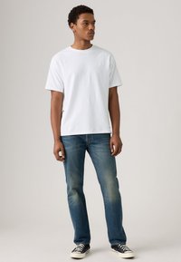 White cotton t-shirt with short sleeves, paired with blue denim jeans. Features a relaxed fit and simple construction, worn with black sneakers.