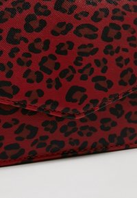 Tissu rouge texturé avec motif léopard noir et coutures visibles sur un bord plié, probablement partie d’un sac à main ou portefeuille.