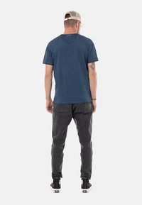 T-shirt en coton bleu avec des manches courtes, un col rond et des détails usés, associé à un pantalon noir fuselé et des baskets montantes noires.