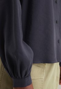 Dunkelblauses Hemd mit gerafften Ärmeln, glatter Textur, Knopfverschluss und entspanntem Schnitt, kombiniert mit hellbeigen Hosen mit Taschen.