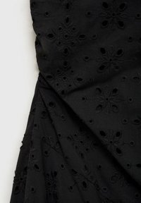 Tissu noir avec broderies florales, présentant des découpes circulaires et une surface texturée. Le tissu semble doux avec un détail de design froncé.