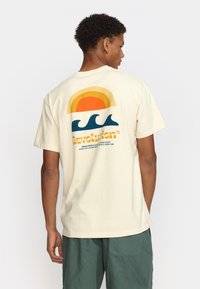 Crème kleurige katoenen t-shirt met een multi-kleurige zonsondergang en golf graphics op de achterkant. Losse pasvorm en korte mouwen.