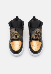 Vysoké tenisky s černým lakovaným svrškem, zlatými akcenty, perforovaným špičkou a výrazným logem s křídly.
