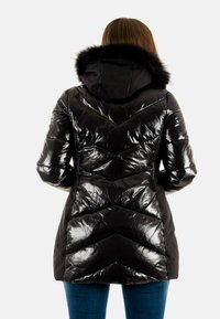 Giacca a vento nera con finitura lucida, motivo a rombi trapuntato, cappuccio con pelliccia, e taglio di lunghezza media. Accenti opachi lungo la cerniera.