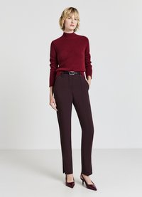 Bordeauxfarbener Rollkragenpullover aus weichem Stoff, kombiniert mit maßgeschneiderten dunklen Hosen mit einem Gürtel. Abgerundet mit passenden spitzen High Heels.