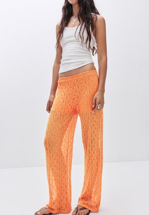 Oranje kanten wijde broek met een zachte, open-gebreide textuur en een elastische tailleband. Draag met een witte tanktop en slippers.