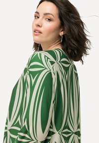 Blusa verde e crema a motivi con un fit rilassato, caratterizzata da audaci motivi a foglia e una texture liscia. Maniche lunghe e scollatura a V.