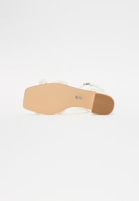 Sandalo bianco conAccenti di perline, design open-toe, tacco basso a blocco e suola beige testurizzata. Dotato di cinturino alla caviglia regolabile.