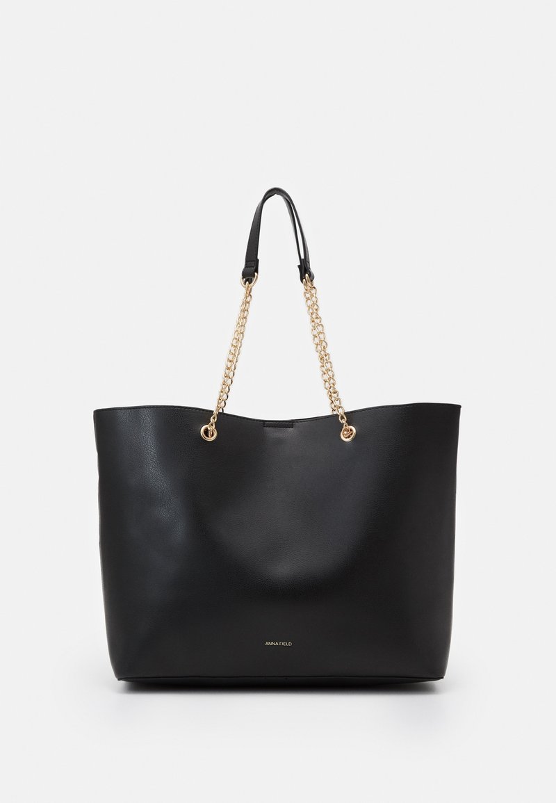 Sac cabas noir avec chaîne dorée et poignées en cuir, texture lisse et petit logo "Anna Field" au centre devant.