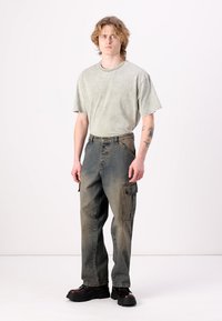 Hellgrünes, übergroßes T-Shirt kombiniert mit dunklen Cargo-Jeans im Stil mit Seitentaschen und einer ausgewaschenen Optik. Schwarze Plateauschuhe.