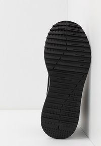Black rubber shoe sole with textured tread pattern and lateral grooves; smooth edges; positioned against a white background.