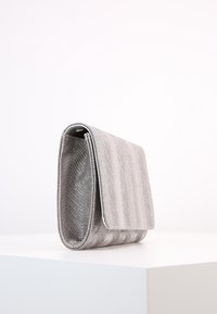 Sølv håndtaske med en struktureret chevron-mønster. Har en fold-over flap og en struktureret form, lavet af et glitrende materiale.