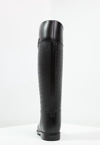 Botas negras hasta la rodilla con un patrón de cocodrilo texturizado en el caña y acentos de cuero liso. Presentan una suela plana y un diseño minimalista.