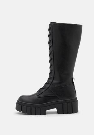 Tall black leather lace-up boot with thick, grooved platform sole and pull tab at the back, shown in side profile.