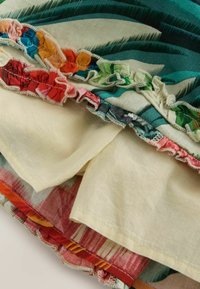 Layered fabric with colorful ruffled edges and a mix of green, red, and cream patterns on lightweight material.