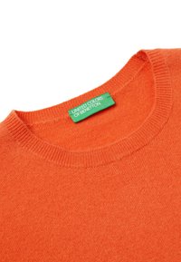 Pomarańczowy sweter z okrągłym dekoltem, z zieloną metką "United Colors of Benetton" wszytą wewnątrz kołnierza.