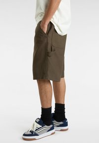 Olivegrüne Cargo-Shorts mit Seitentaschen und lockerer Passform, aus robustem Material. Getragen mit navyblauen Turnschuhen und schwarzen Socken.