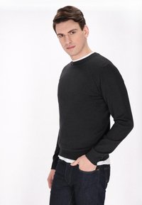 Fekete kötött pulóver kerek nyakkal, hosszú ujjakkal és slim fit fazonnal, sötét farmernadrággal párosítva. Simára kidolgozott anyag, minimális részletekkel.