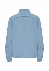 Ljusblå jacka tillverkad av strukturerat material. Har en hög krage, elastiska ärmslut och kontrasterande piping längs sömmarna.