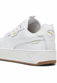 Vita låga sneakers i syntetiskt läder med textur, med en guldfärgad Puma-logga och gummigummisula, designade med subtila sömnadsdetaljer.