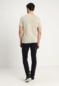 T-shirt aderente beige chiaro con maniche corte e scollatura rotonda. Abbinata a pantaloni neri slim-fit e sneakers nere. Design semplice, texture liscia.
