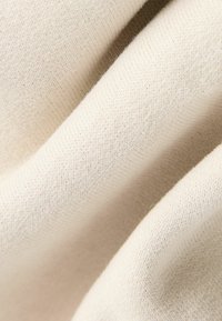 Cremefarbener Strickstoff mit einer glatten Textur, der ein feines Rippmuster aufweist. Das Material wirkt weich und leicht dehnbar.