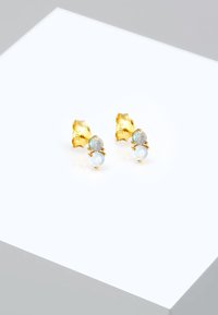 Guldtonet stud øreringe med lyseblå sten og en tekstureret bagside. Designet er elegant med rundede former og en poleret finish.