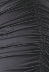 Čierna nariadená látka na detailnom zábere s hladkým povrchom a zhromaždenými časťami vytvárajúcimi vzor záhybov. Žiadne ďalšie detaily nie sú viditeľné.