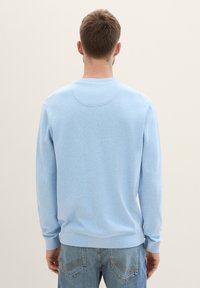 Helles blaues Sweatshirt mit langen Ärmeln, rundem Hals und gerippten Bündchen. Weiche Textur und einfaches Design ohne sichtbare Logos. Getragen mit blauen Jeans.