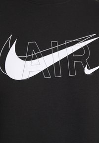Musta puuvillainen T-paita, jossa on näkyvä valkoinen "AIR"-logo ja Nike Swoosh -kuvake, graafisilla viivoilla ja modernilla kirjasintyylillä.