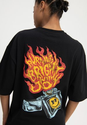 Zwart oversized T-shirt met een vurige rood-gele afbeelding met tekst en een cartoonaansteker illustratie op de achterkant.