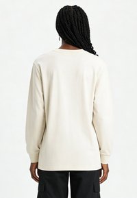 T-shirt à manches longues en coton beige clair avec un col rond, présentant une coupe décontractée et une texture lisse. Aucun logo ou motif visible.