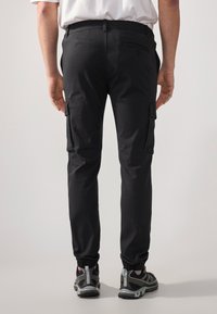 Pantaloni cargo neri con cintura e polsini elasticizzati. Presentano tasche laterali con patta e una tasca posteriore. Realizzati in un tessuto resistente.