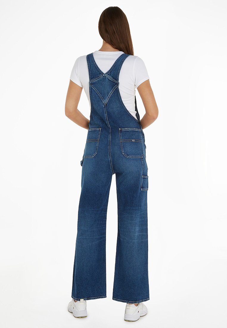 Salopette en denim à pattes larges, avec des bretelles ajustables, un empiècement au dos et plusieurs poches. Couleur bleu foncé avec un léger décoloré.