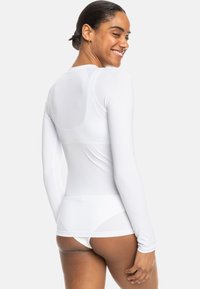Long-sleeve, form-fitting white top made of smooth, lightweight fabric. Features a rounded neckline and seamless design at the back.