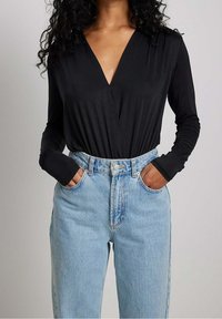 Top nero a maniche lunghe con scollo a V profondo, abbinato a jeans in denim leggeri a vita alta. Tessuto liscio con una silhouette aderente.