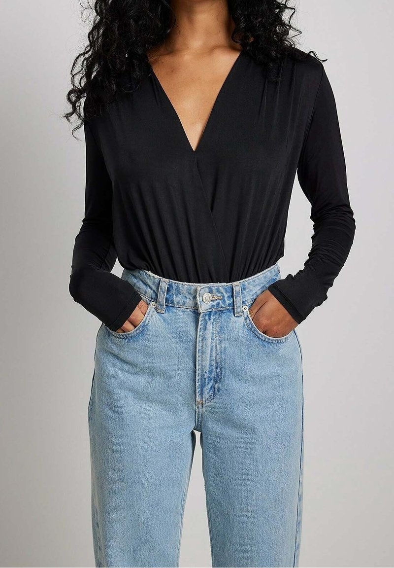 Top nero a maniche lunghe con scollo a V profondo, abbinato a jeans in denim leggeri a vita alta. Tessuto liscio con una silhouette aderente.