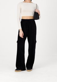 Zwarte corduroy cargo broek met brede pijpen en zijzakken, gecombineerd met een crème lange mouw cropped top. Voorzien van een stijlvolle zwarte handtas.