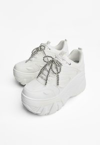 Vita plattformssneakers i slätt läder med rund tå, framträdande sömmar, texturerade sålar och dekorativa snören med silverpärlor.