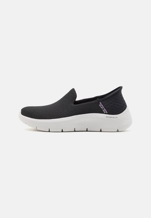 Czarny sportowy but wsuwany z białą grubą podeszwą, siateczkową cholewką i etykietą "Skechers Slip-Ins" z boku.