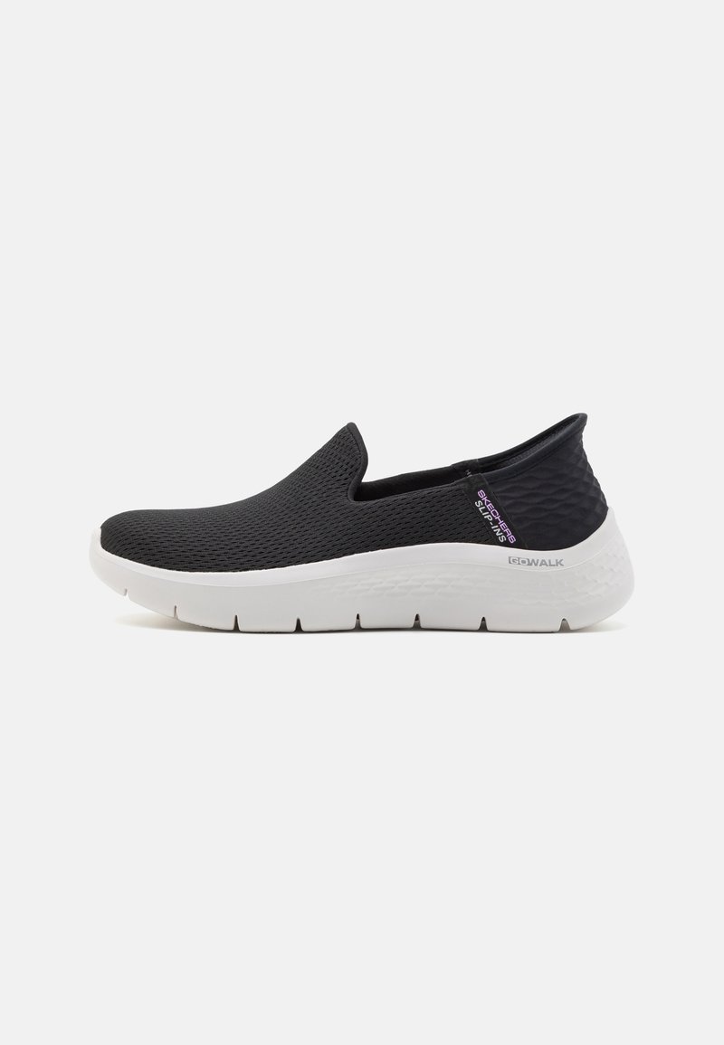Chaussure de sport noire à enfiler avec semelle blanche épaisse, dessus en mesh et étiquette "Skechers Slip-Ins" sur le côté.