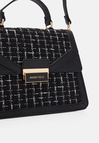 Svartvitt vävt handväska med texturerad yta, utrustad med ett guldspänne och svarta läderdetaljer. Dubbla handtag och justerbar rem.