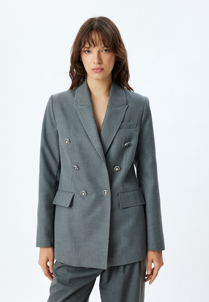 Grijze dubbelgeknoopte blazer met zilveren knopen, opstaande revers, twee voorzakken en een getailleerde pasvorm. Soepele textuur, gestructureerd ontwerp.
